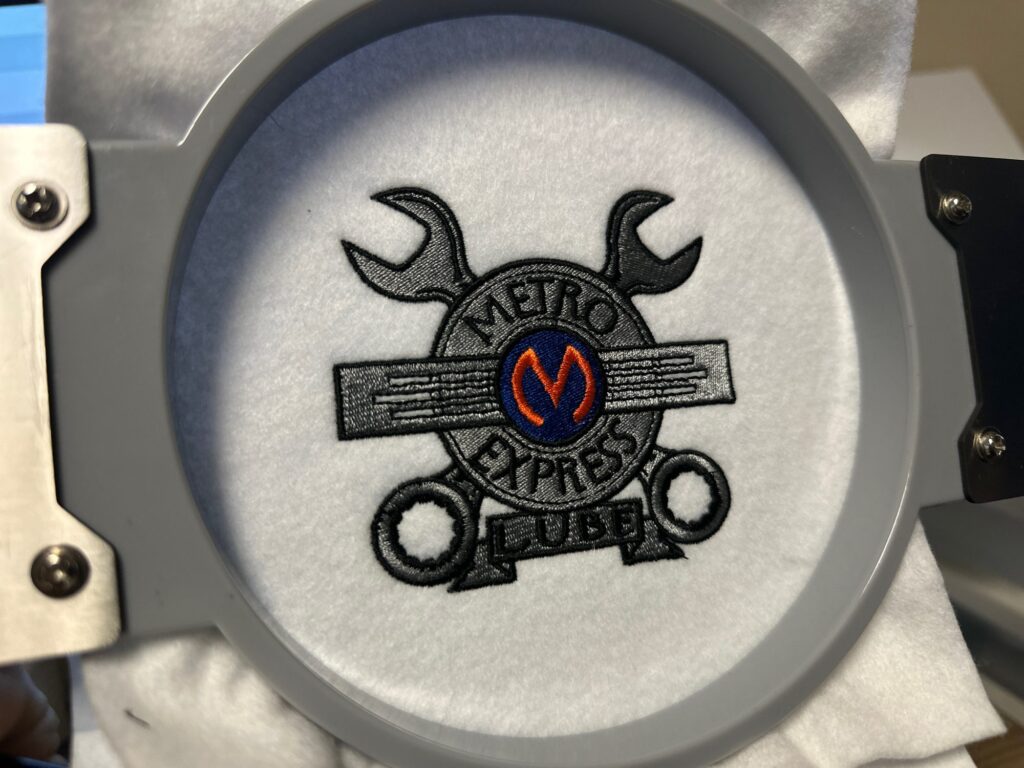 Custom logo embroidery for a local car shop still on the hoop at The Print Plug embroidery shop in Nampa