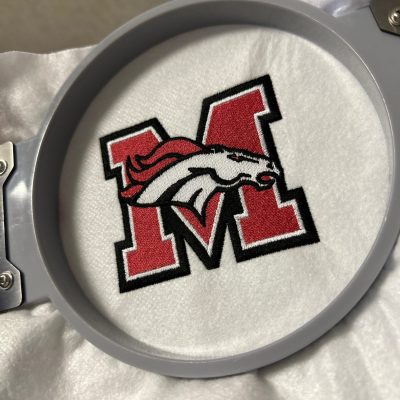Custom embroidered logo for a local school organization, still on the hoop at The Print Plug embroidery shop