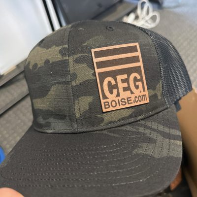 Custom faux leather patch on the left panel of camo baseball hats at The Print Plug in Nampa